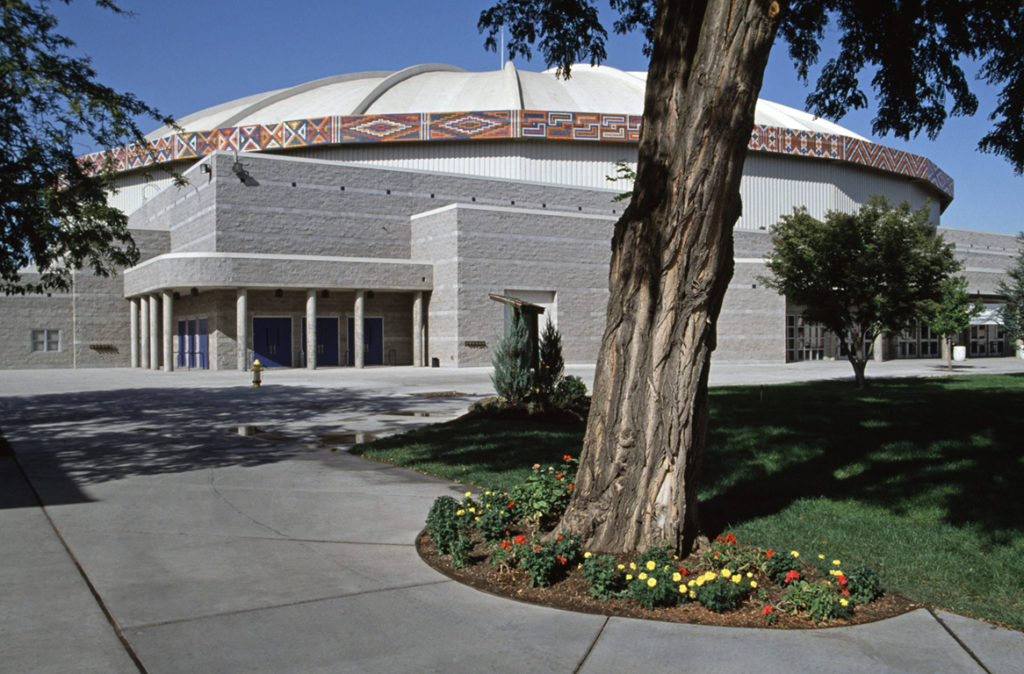 A band of geometric patterns made of thousands of 3-inch industrial highway reflectors encircles the circular roof of a large concrete building. There is a very blue sky behind the SunDome.