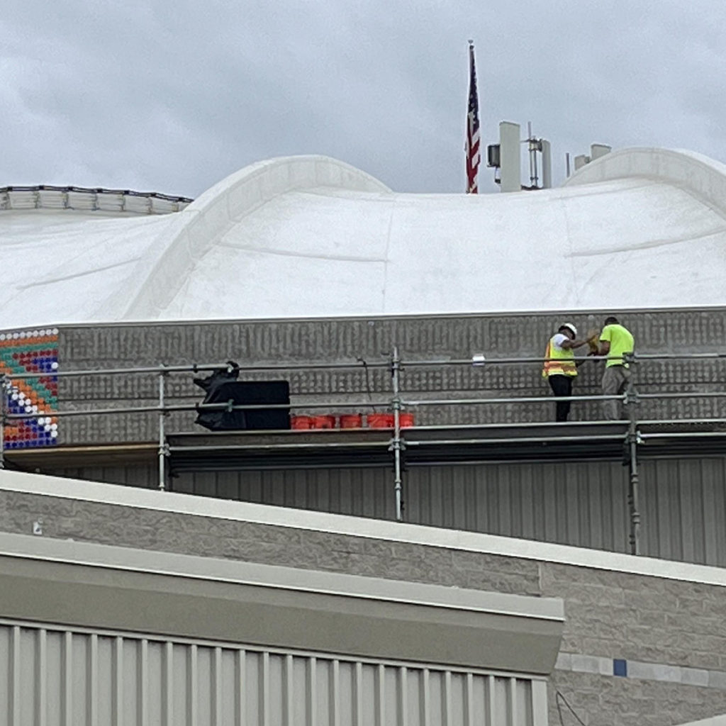 Workers on scaffolding clean the concrete surface of the SunDome