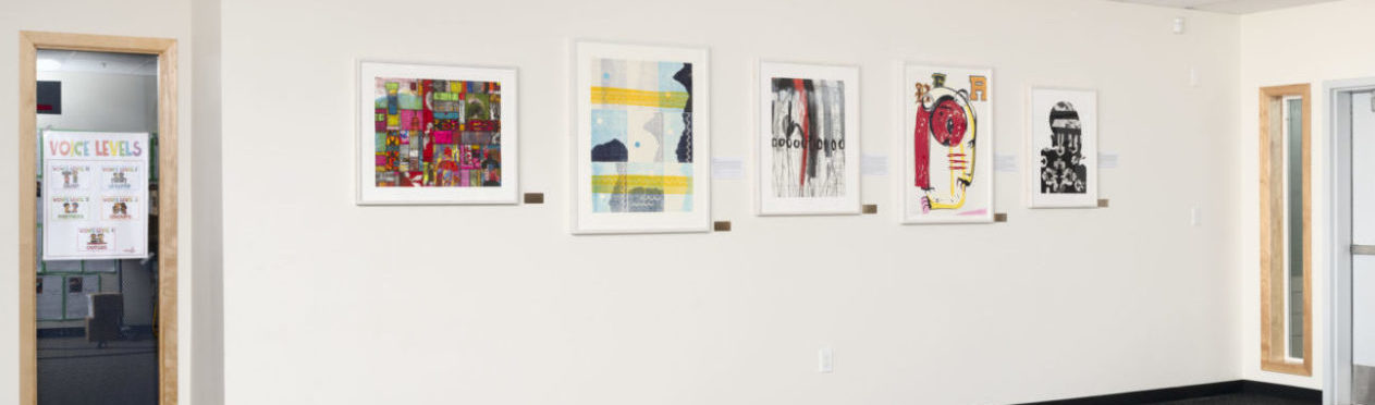 Four colorful, abstracted artworks hang on a cream wall in an elementary school hallway.